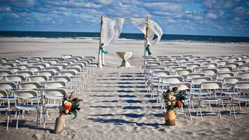 A beach wedding setup with chairs arranged in rows, a canopy, and floral centerpieces.