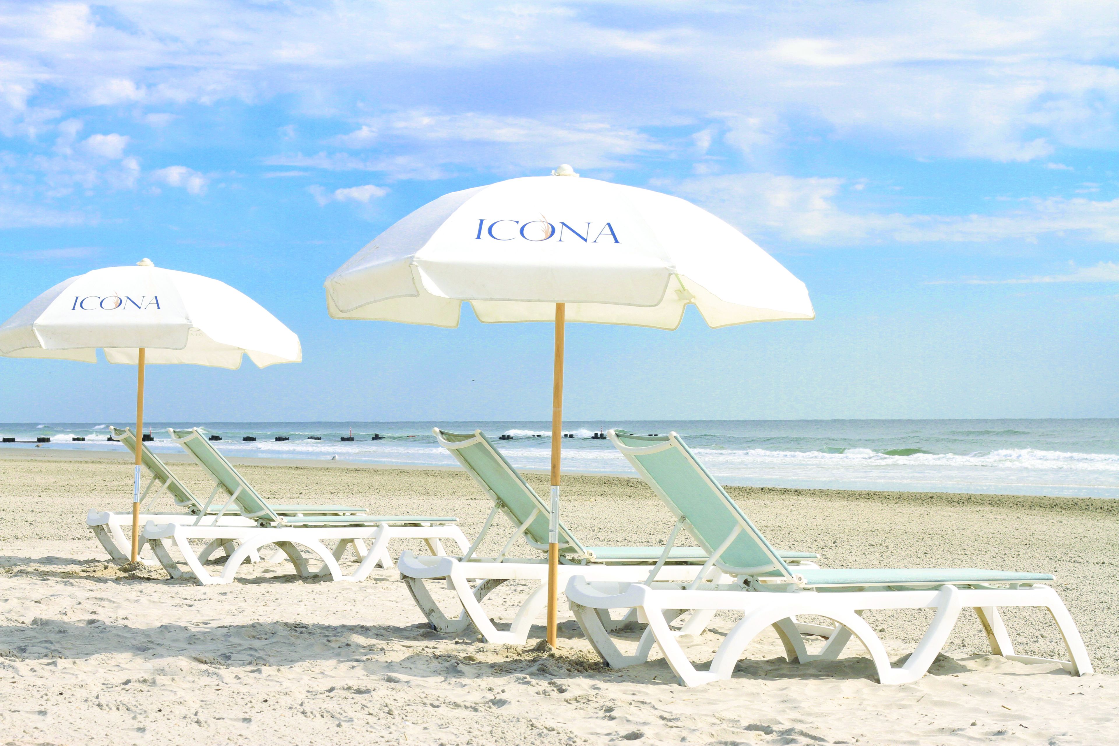 Beach chairs and white ICONA umbrellas on a sandy beach with the ocean in the background.