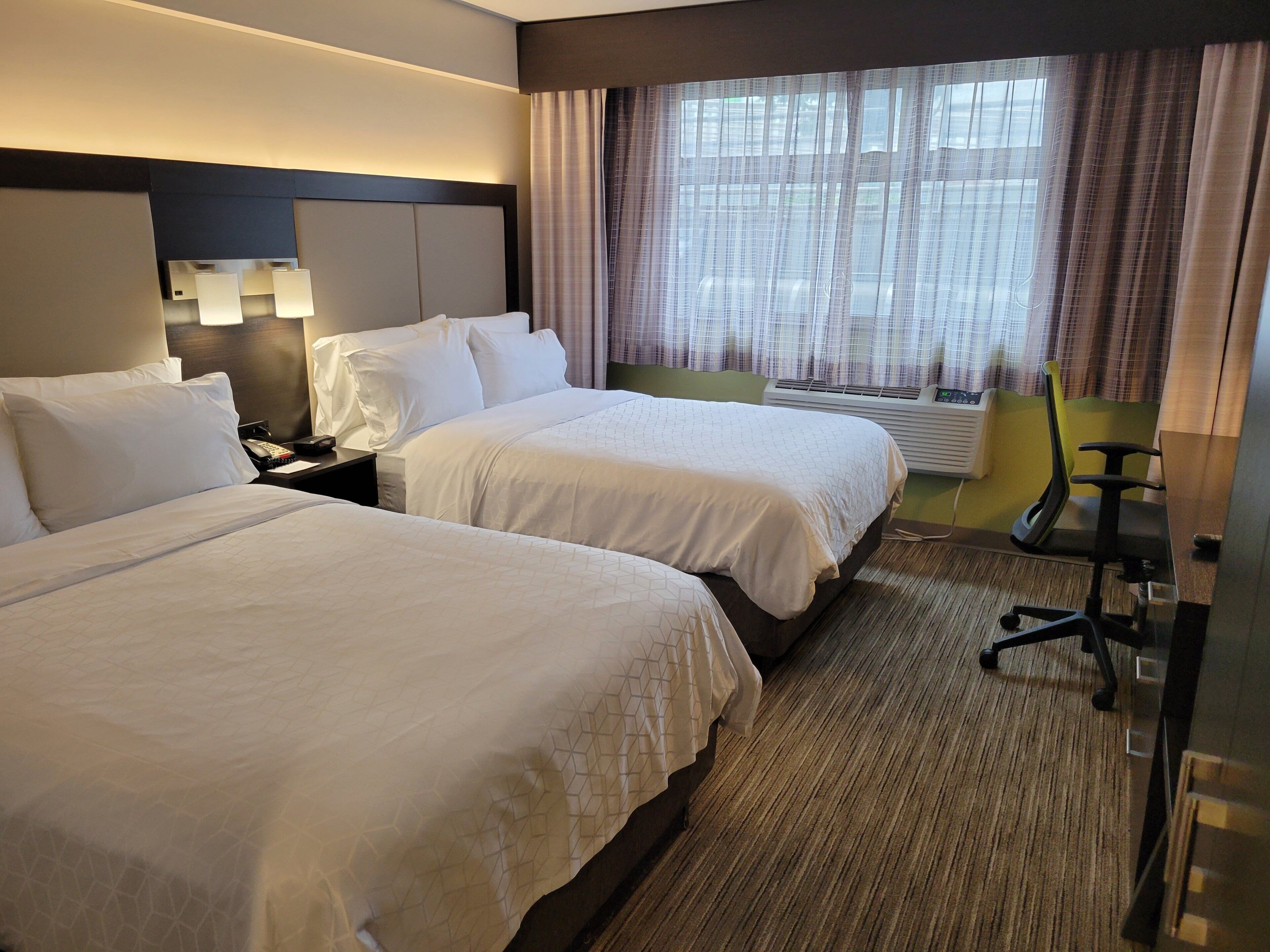 A hotel room with two beds, a desk, a chair, and a window with curtains.