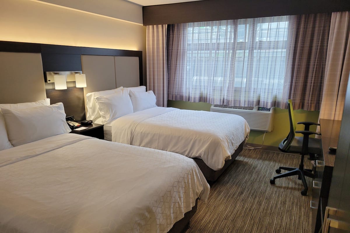 A hotel room with two beds, a desk, a chair, and a window with curtains.