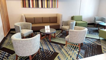 A hotel lobby with a brown sofa, multiple armchairs, a small table, and a patterned carpet.