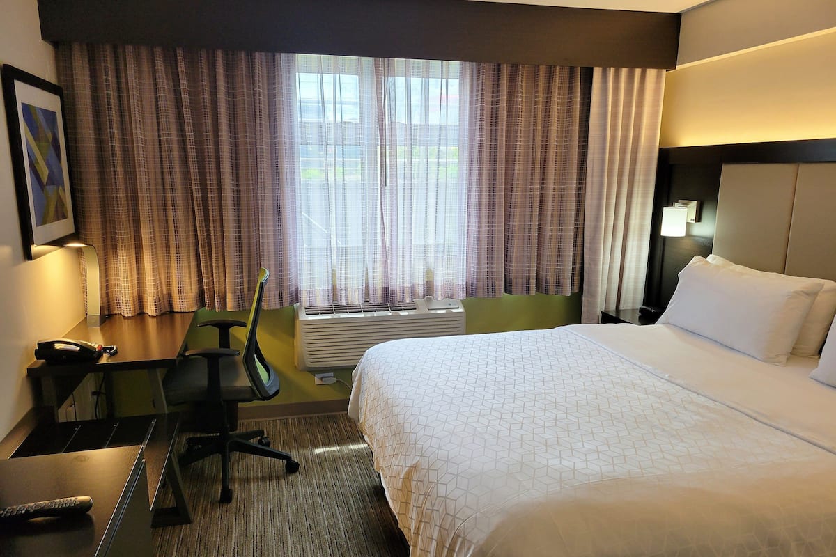 A hotel room with a bed, desk, chair, and a window with curtains.