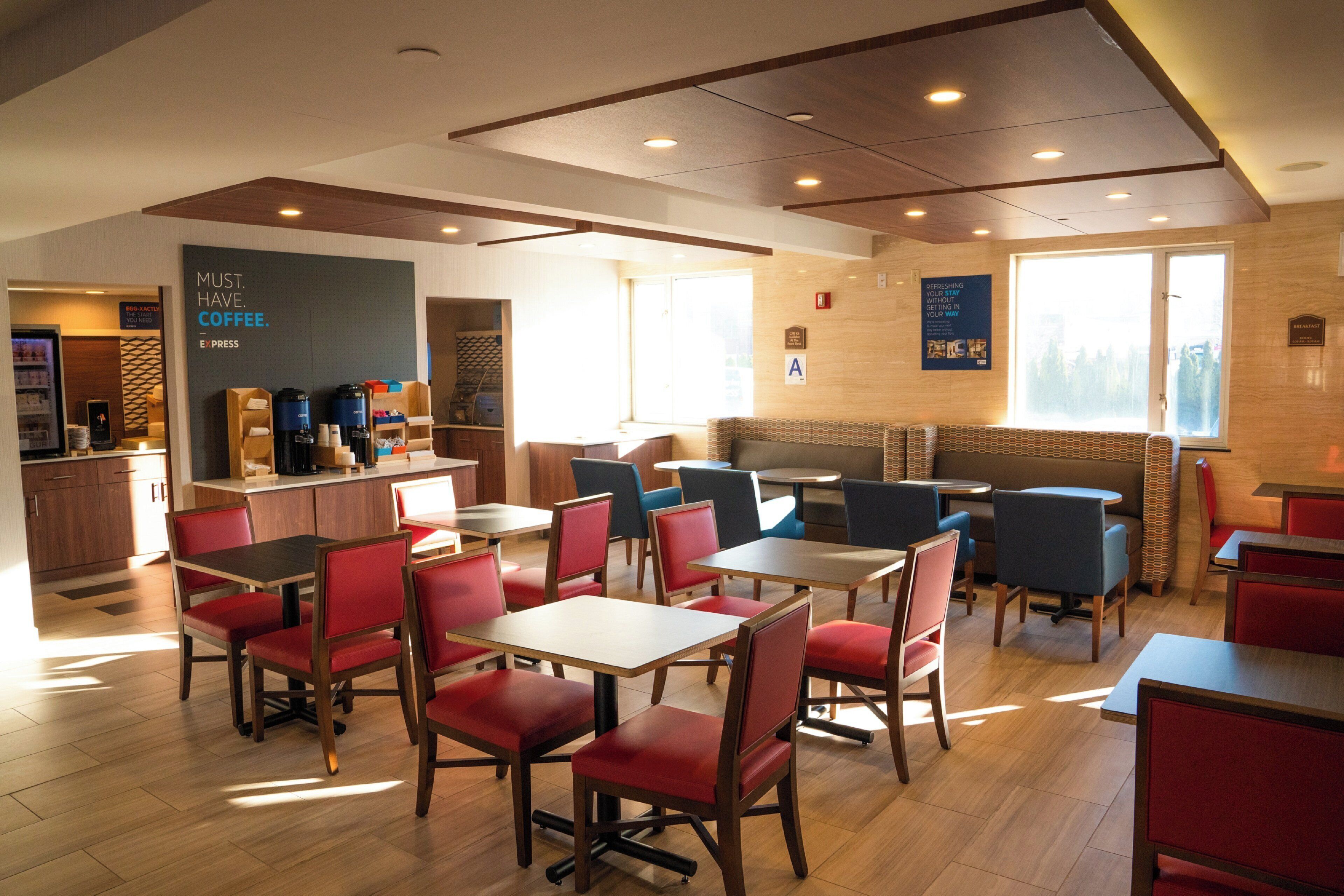 A modern cafe with wooden tables and chairs, a coffee station, and a seating area with a view.