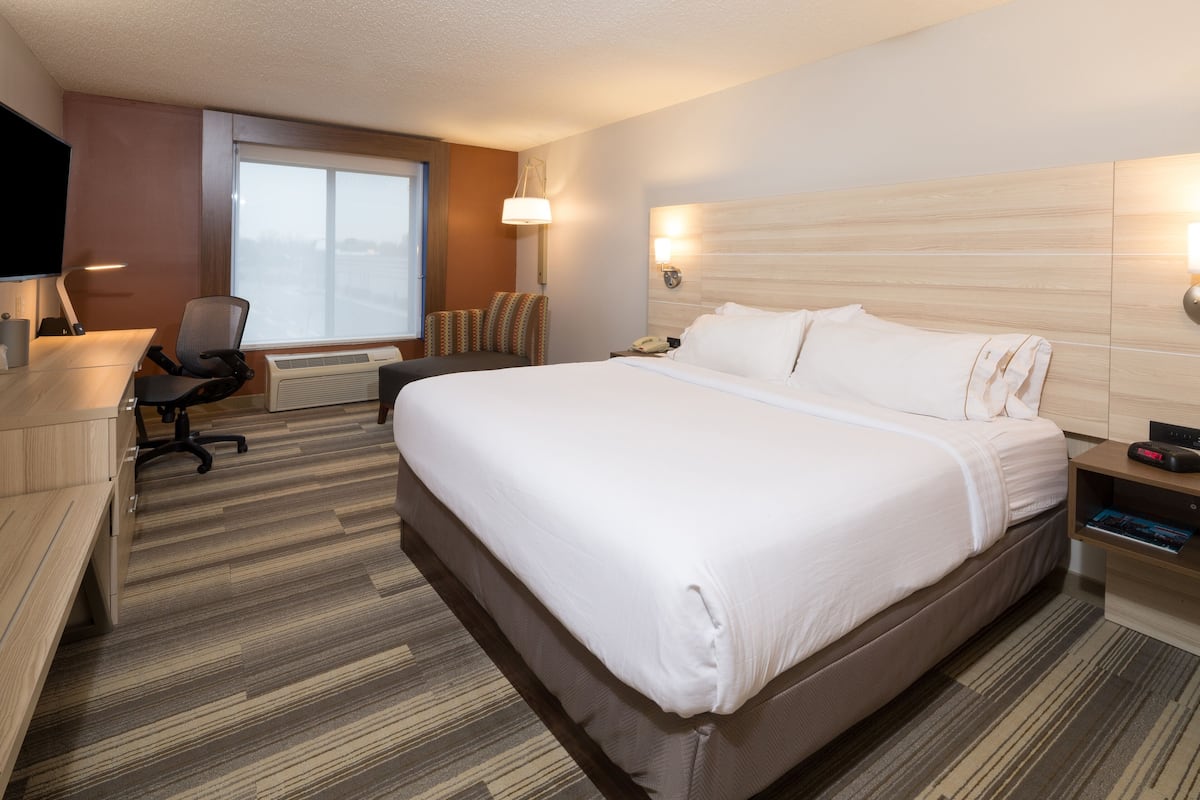 A hotel room with a large bed, a desk with a chair, a TV, and a window with blinds.