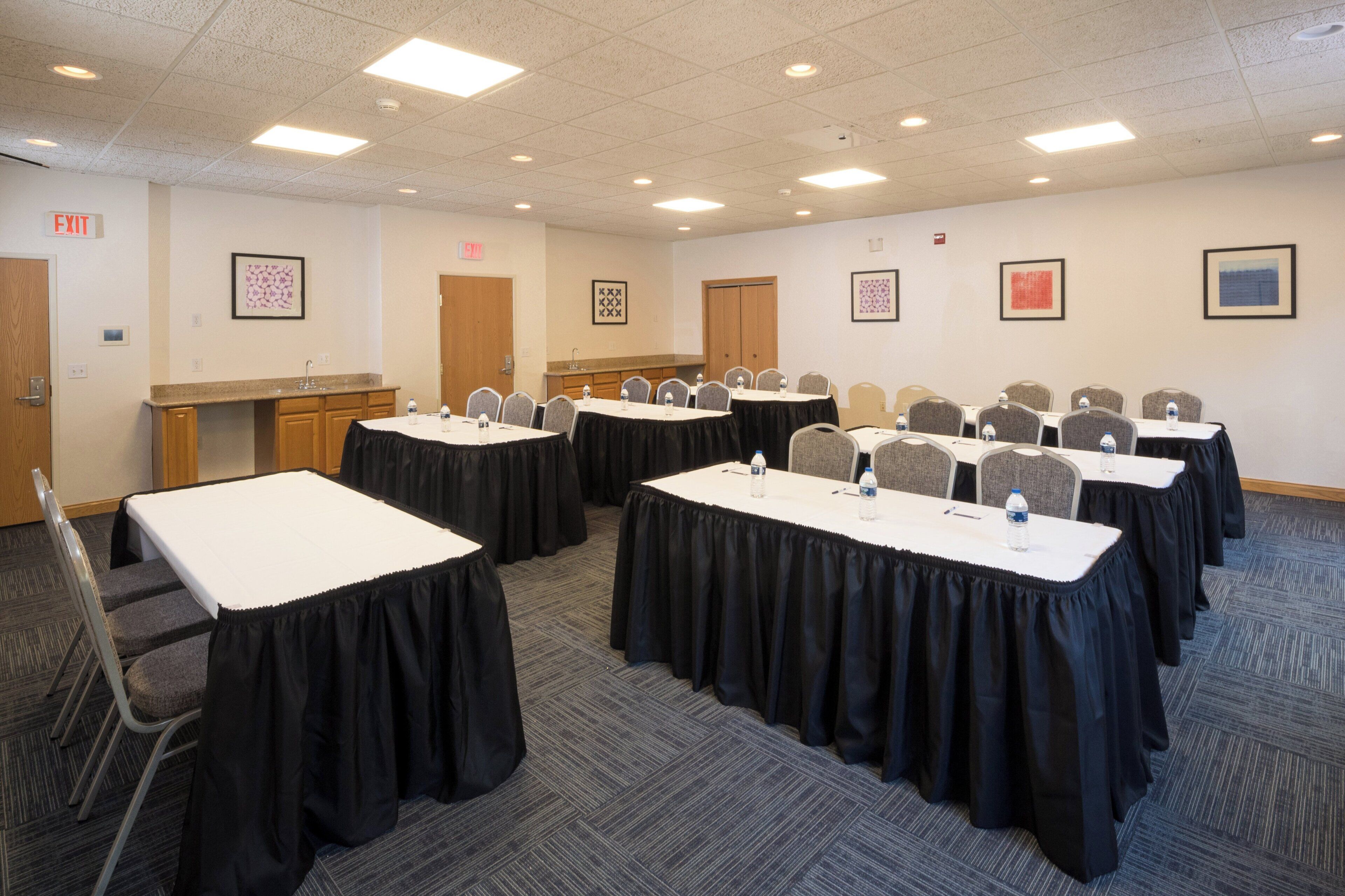 A conference room with multiple tables, chairs, and a kitchenette area.