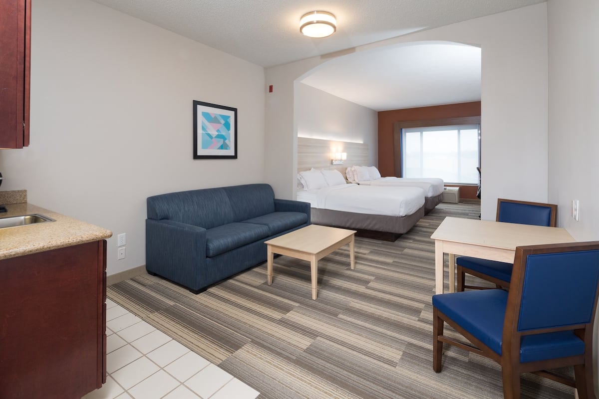 A hotel room with a kitchenette, a sofa, a small table, a bed, and a chair.