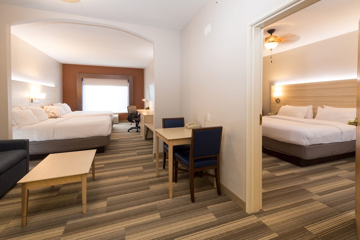 A hotel room with two beds, a desk, a chair, a small table, and a sofa.