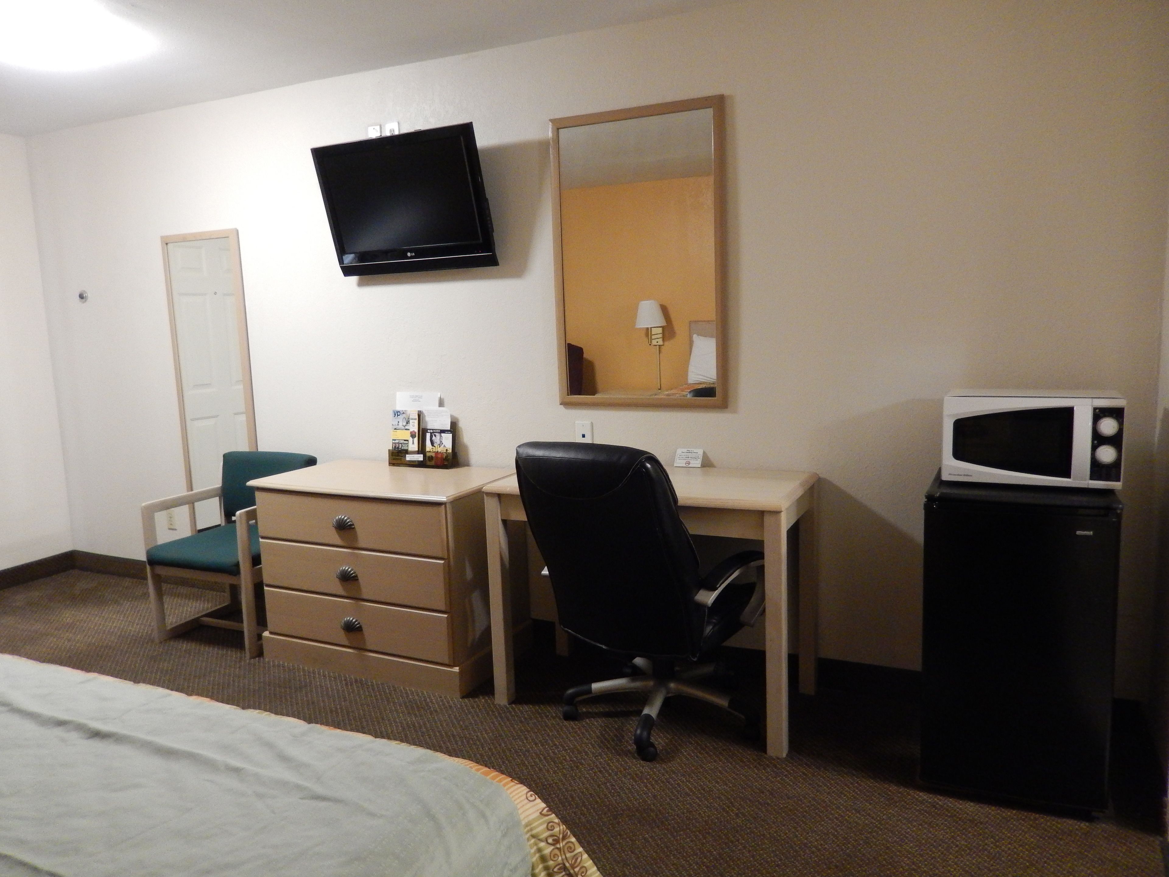 Habitación de hotel con cama, escritorio, silla, televisor, espejo y microondas.