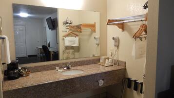 A bathroom with a granite countertop, a sink, a mirror, a hairdryer, and a towel rack.