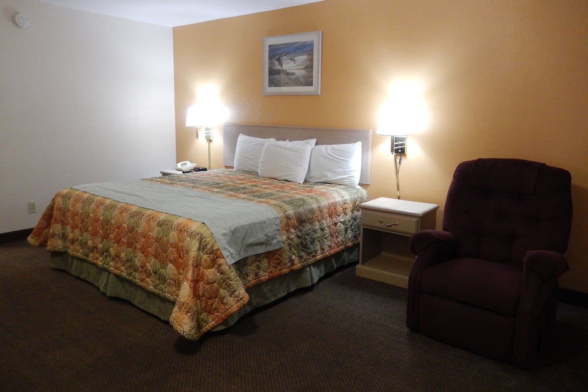Une chambre d’hôtel avec un lit, deux lampes de chevet, une chaise et un tableau au mur.