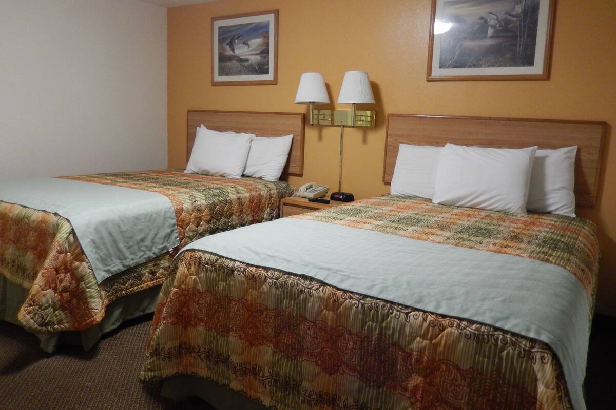 Une chambre d’hôtel avec deux lits, chacun recouvert d’une couvre-lit à motifs, une table de chevet avec un téléphone et deux lampes fixées au mur.