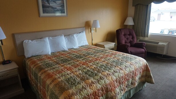 Ein Hotelzimmer mit einem großen Bett, zwei Nachttischen, einem Sessel, einer Lampe und einem fenster mit Vorhängen.