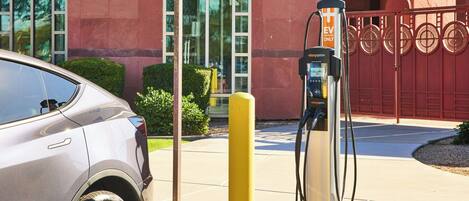 Un coche plateado estacionado en una estación de carga para vehículos eléctricos, con un edificio al fondo.