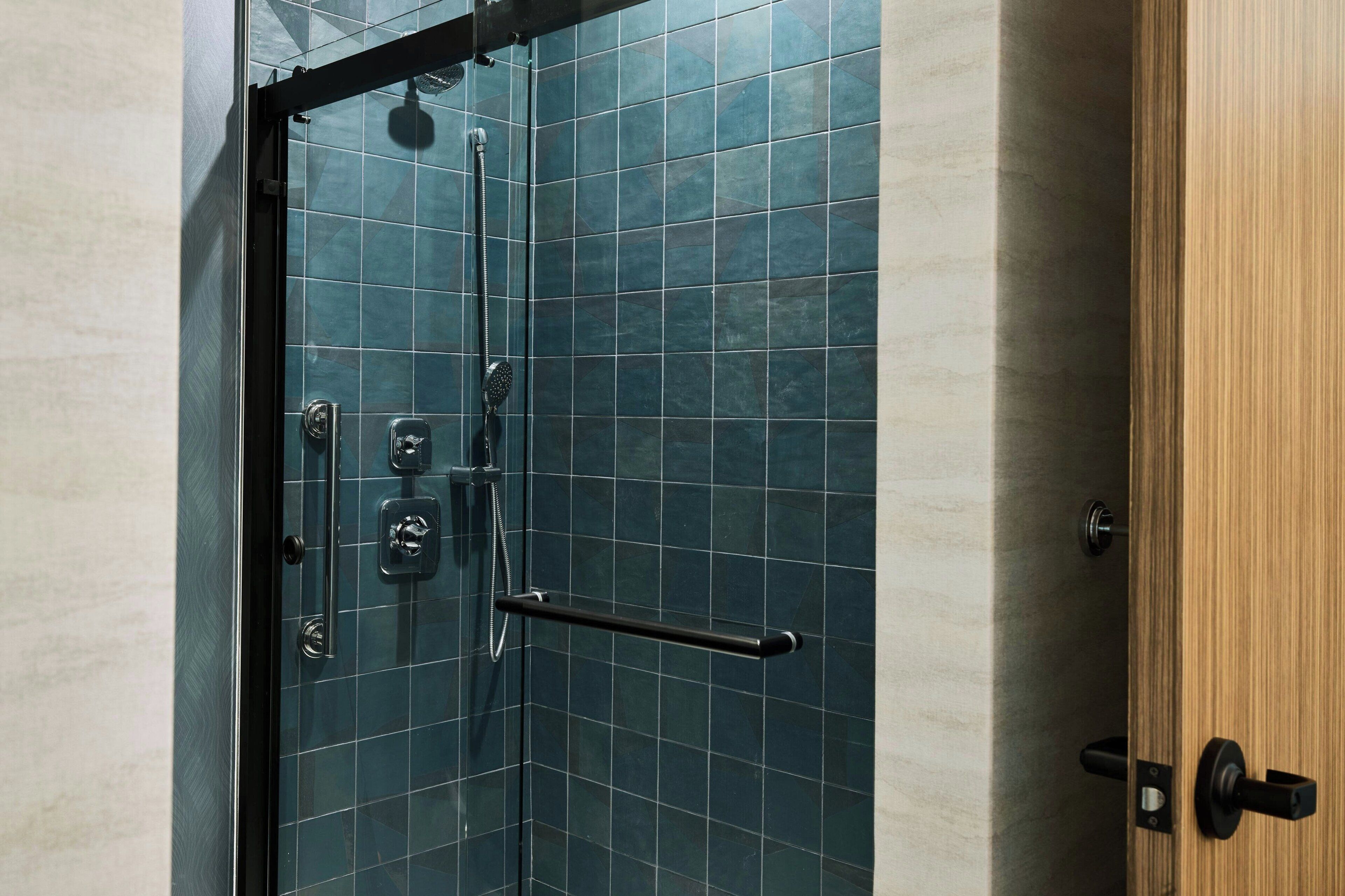 A glass-enclosed shower with a black handle and a towel bar.
