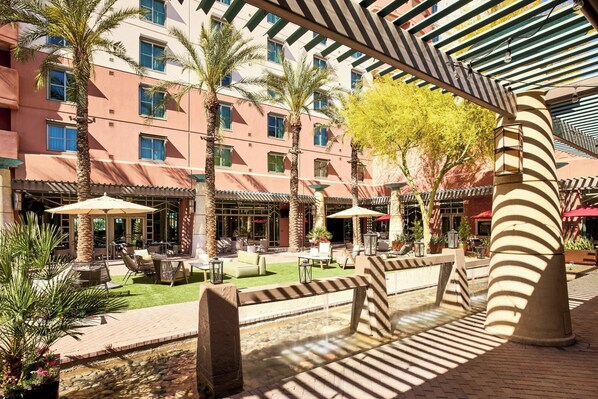 Relax in a serene outdoor courtyard with shaded seating areas, lush greenery, and a soothing water feature.