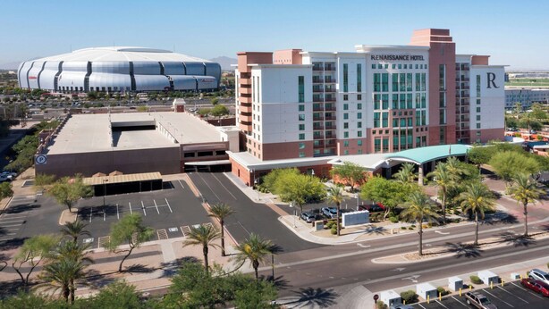 A Renaissance Hotel with a modern design, featuring a prominent 'R' on the facade, a parking lot, and a large stadium in the background.