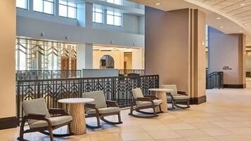 A spacious lobby with high ceilings, a mezzanine level, and a view of the interior. There are several rocking chairs and round tables arranged for seating.