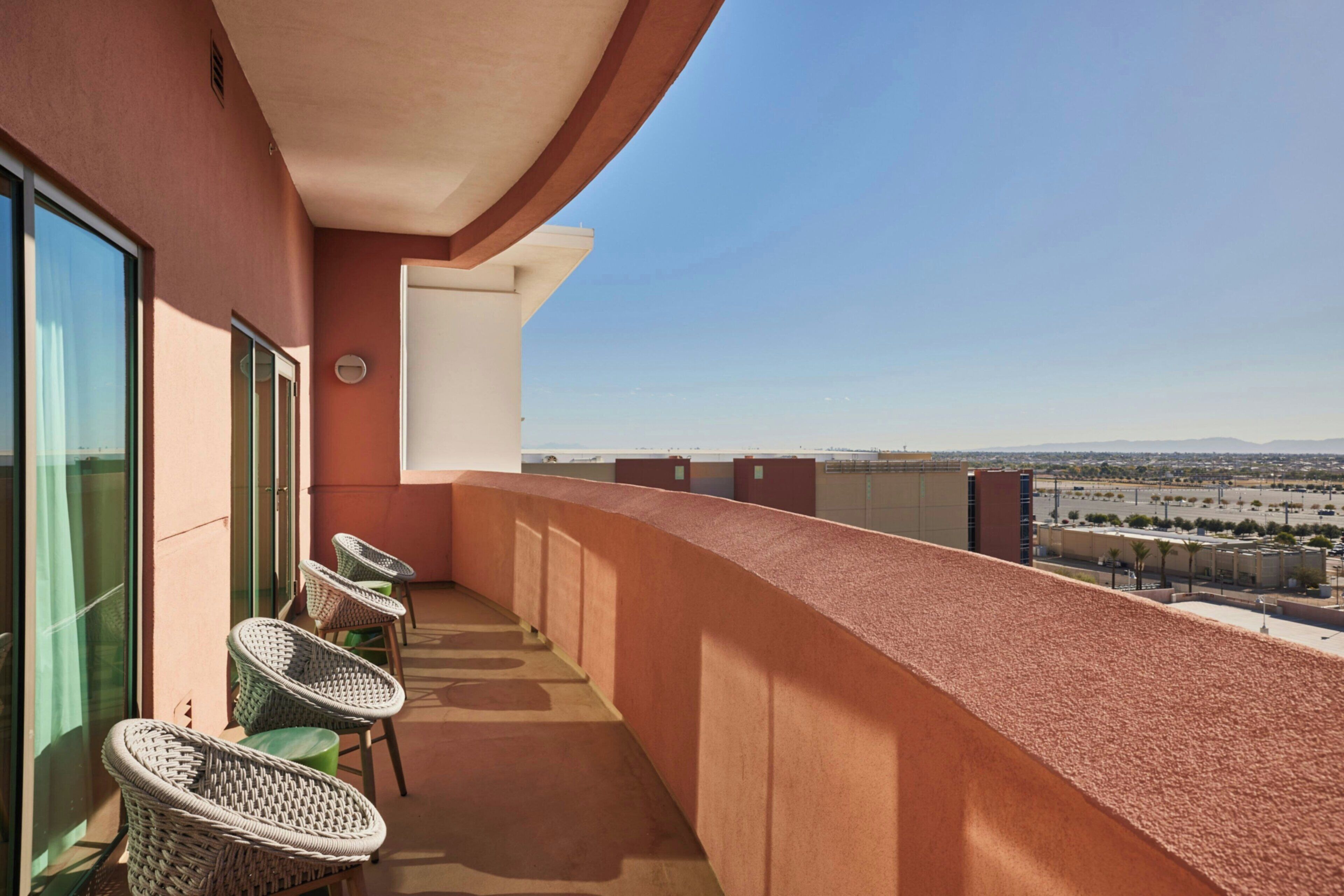 A balcony with wicker chairs, a glass door, and a view of a cityscape.