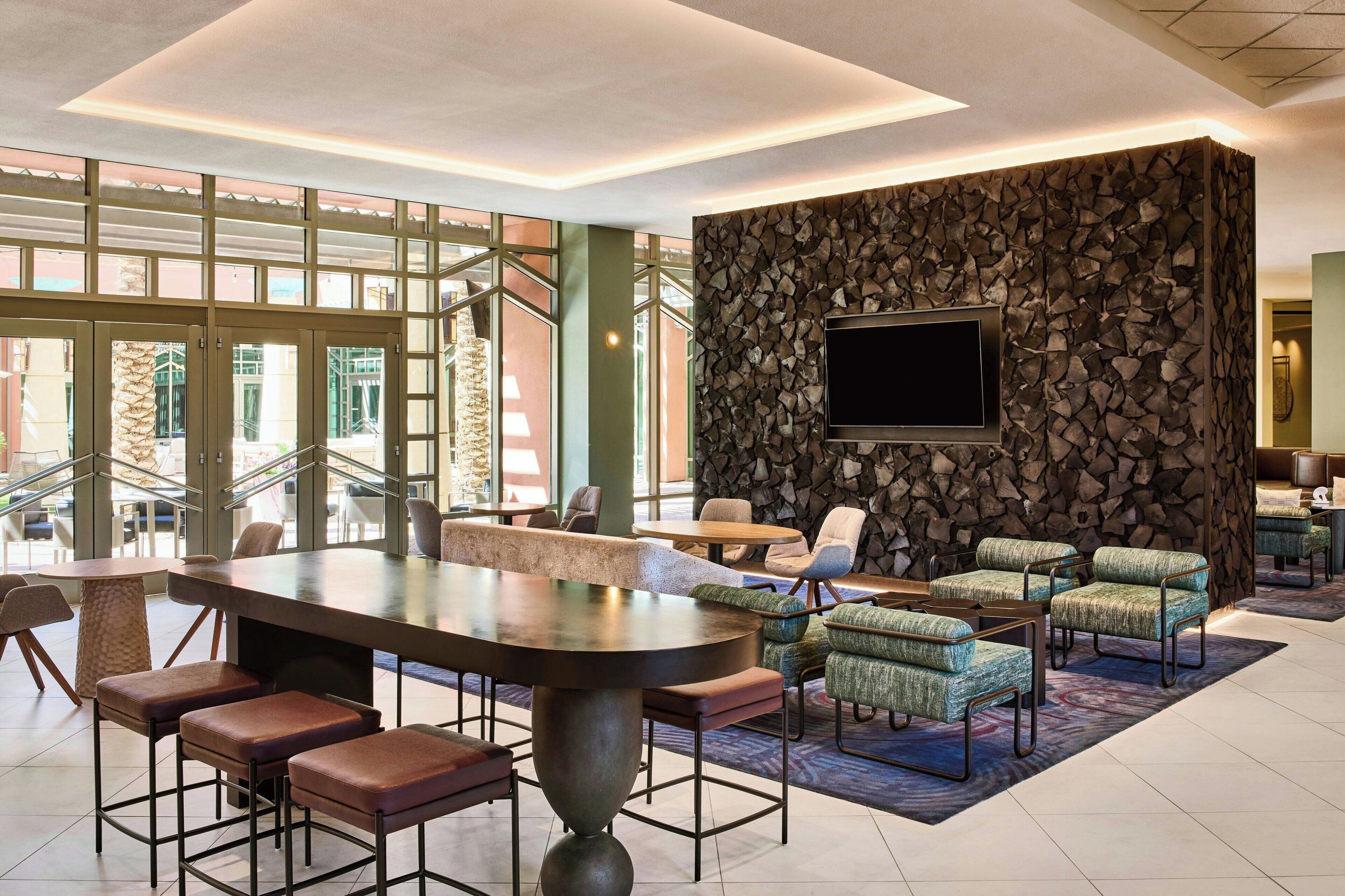 A modern lobby with a large bar area, seating, and a stone wall with a TV.