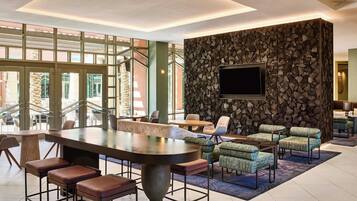 A modern lobby with a large bar area, seating, and a stone wall with a TV.