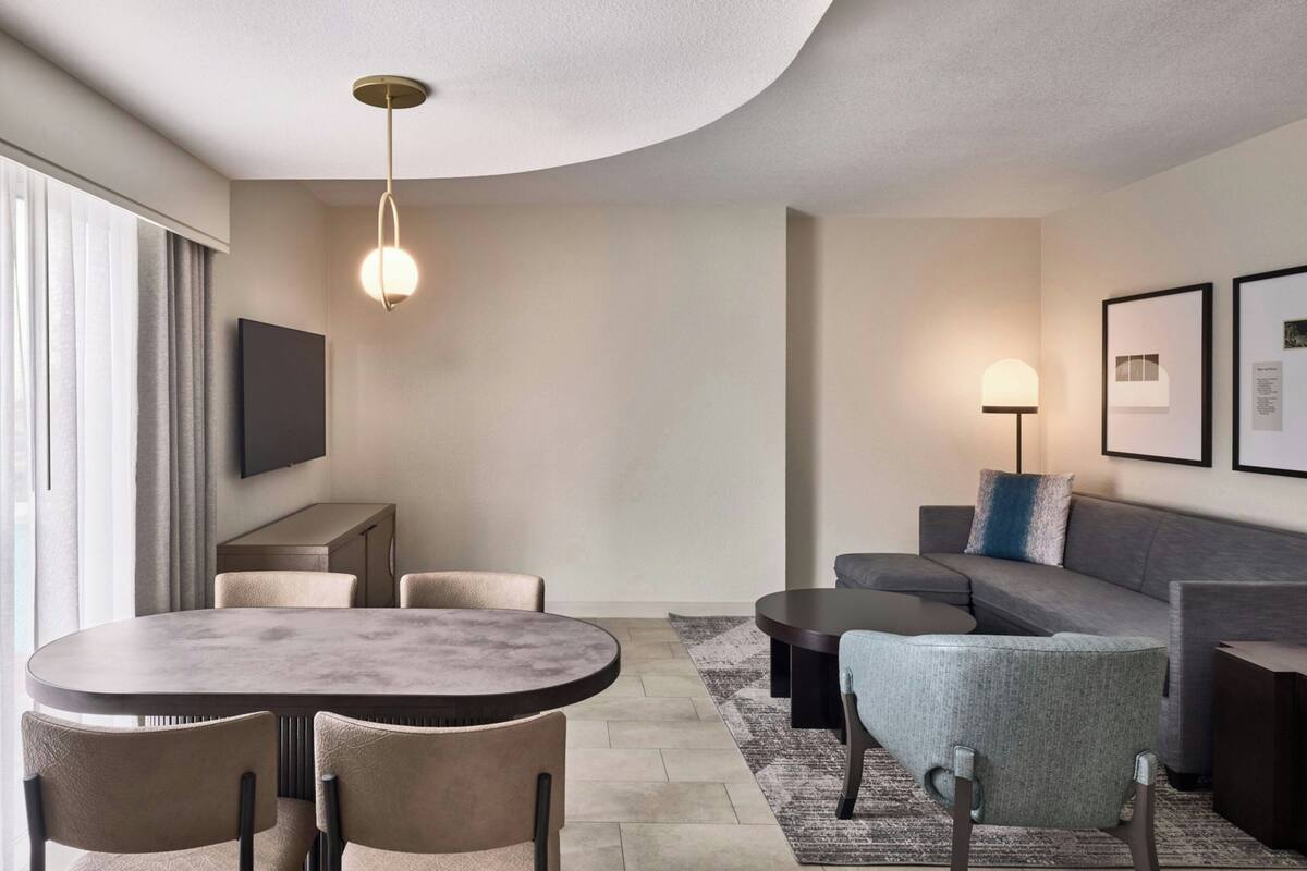 Ein modernes Wohnzimmer mit einem runden Esstisch, zwei Sofas, einem an der Wand montierten Fernseher und einer Deckenleuchte.