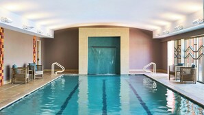 An indoor swimming pool with a tiled wall, benches, and a ceiling with recessed lighting.