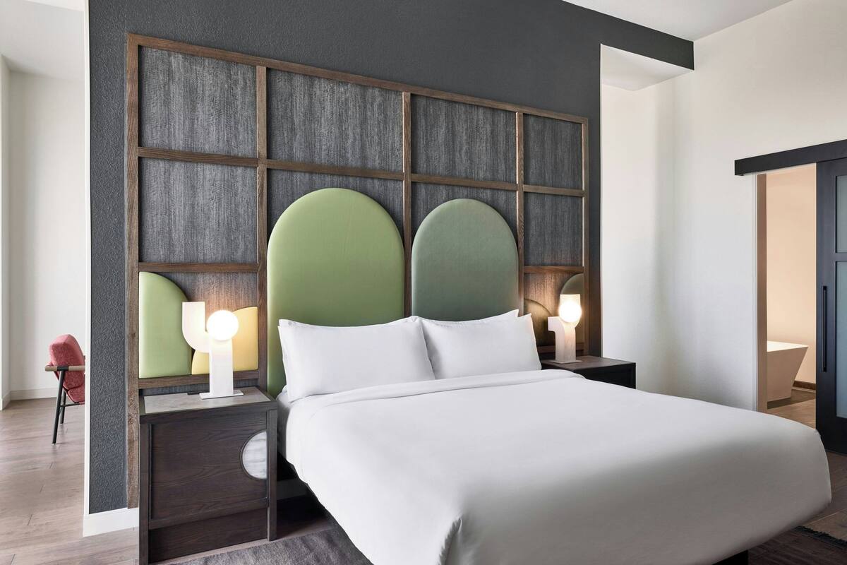 Ein modernes Hotelzimmer mit einem großen Bett, zwei Nachttischen mit Lampen und einem außergewöhnlichen Kopfteil.