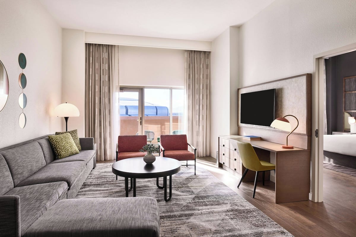 Ein modernes Hotelzimmer mit einer Couch, zwei Sesseln, einem Couchtisch, einem Schreibtisch und einem Fernseher.