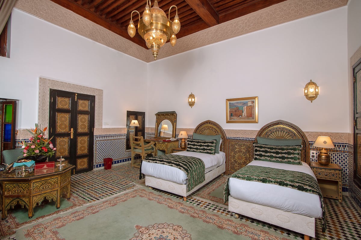 A traditional Moroccan room with a large bed, a wooden desk, and a chandelier.