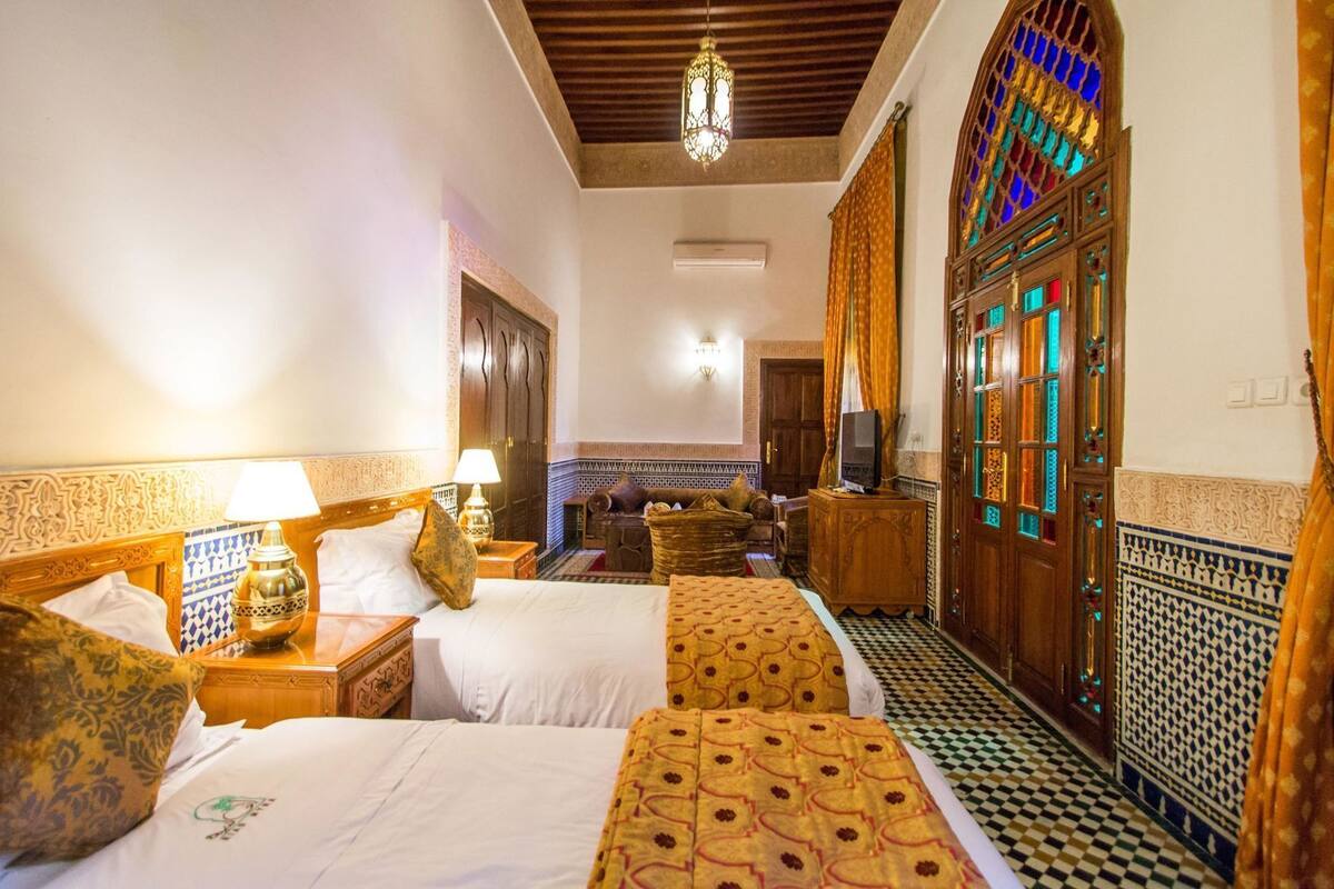 A hotel room with two beds, a television, a decorative wall, and a patterned floor.
