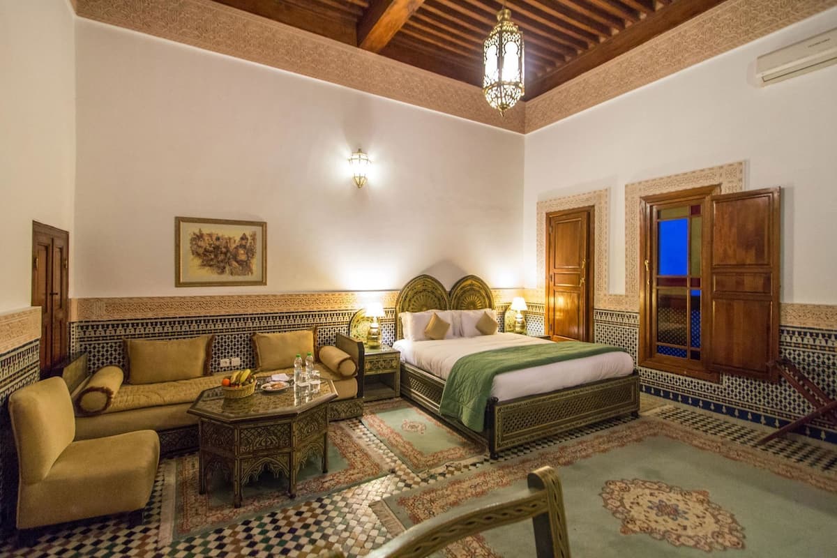 A traditional Moroccan room with a bed, sofa, and coffee table, featuring intricate tile work and wooden furniture.