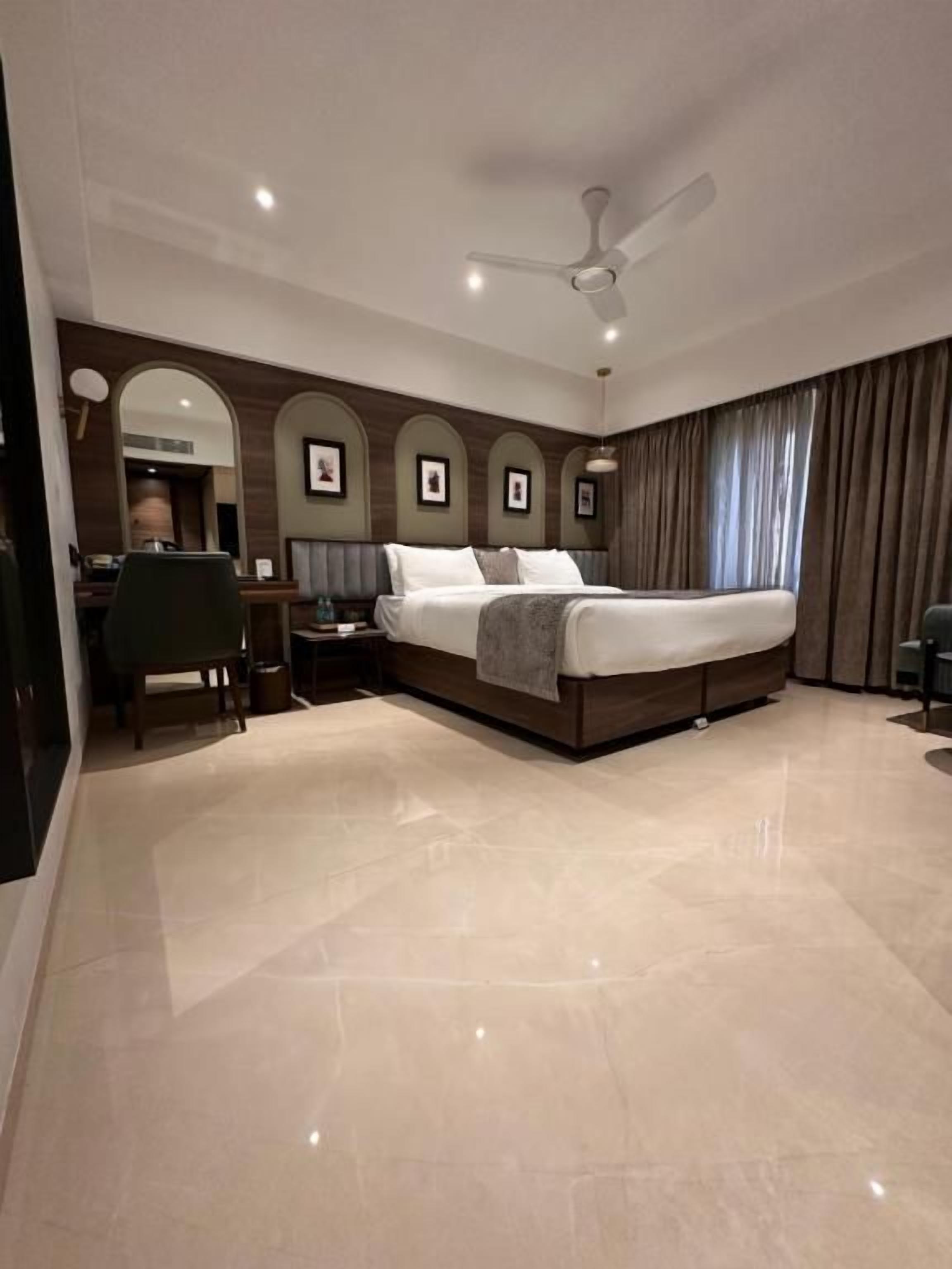 A modern hotel room with a large bed, a desk, and a ceiling fan.