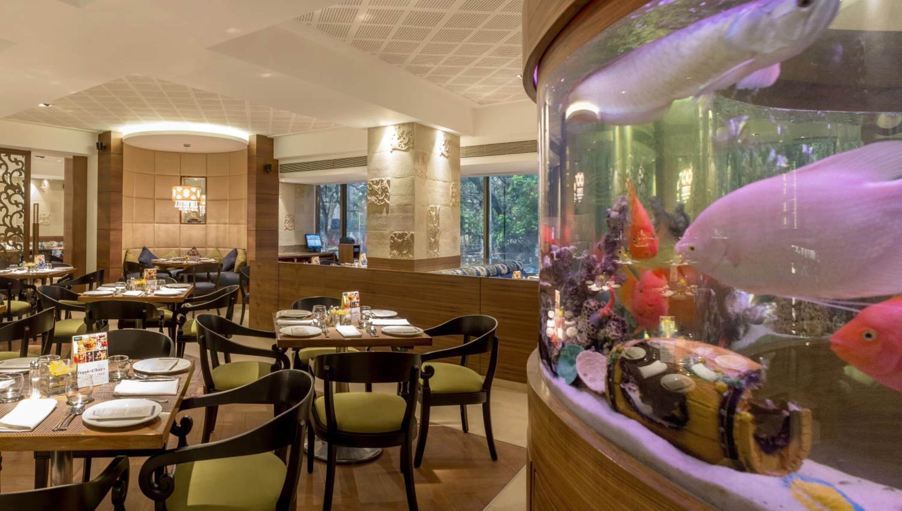 Een restaurant met gedekte tafels, een aquarium met kleurrijke vissen en uitzicht op het omliggende landschap.