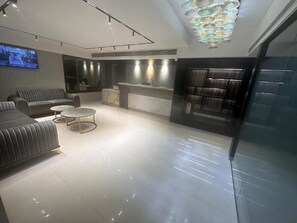 A modern hotel lobby with a sofa, a round coffee table, a reception desk, and a television screen. - The International by Tunga (Mumbai)