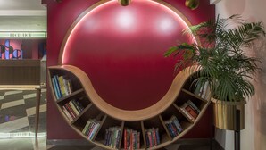 A modern reception area with a red wall, a curved bookshelf filled with books, and a potted plant. - T24 Retro (Mumbai)