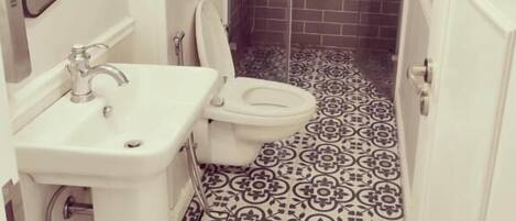 Un baño con lavamanos blanco, inodoro y zona de ducha con mampara de vidrio.