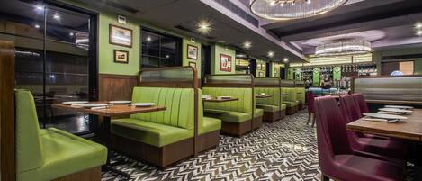 Un restaurante con asientos tipo banca verdes, mesas de madera y suelo con estampado.