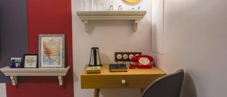 A room with a desk, a chair, a shelf with books and a red telephone, and a wall-mounted light.