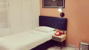 A bedroom with a bed, a nightstand, a lamp, a trash bin, and a framed picture on the wall.