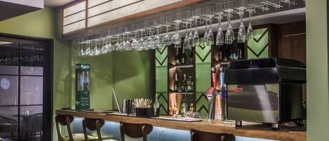 A bar area with a counter, stools, hanging glasses, and a coffee machine.