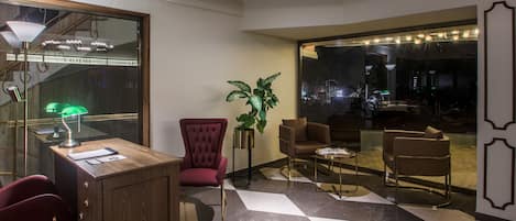 Een moderne lobby met een houten receptiebalie, een rode fauteuil en een glazen scheidingswand met uitzicht over de stad.