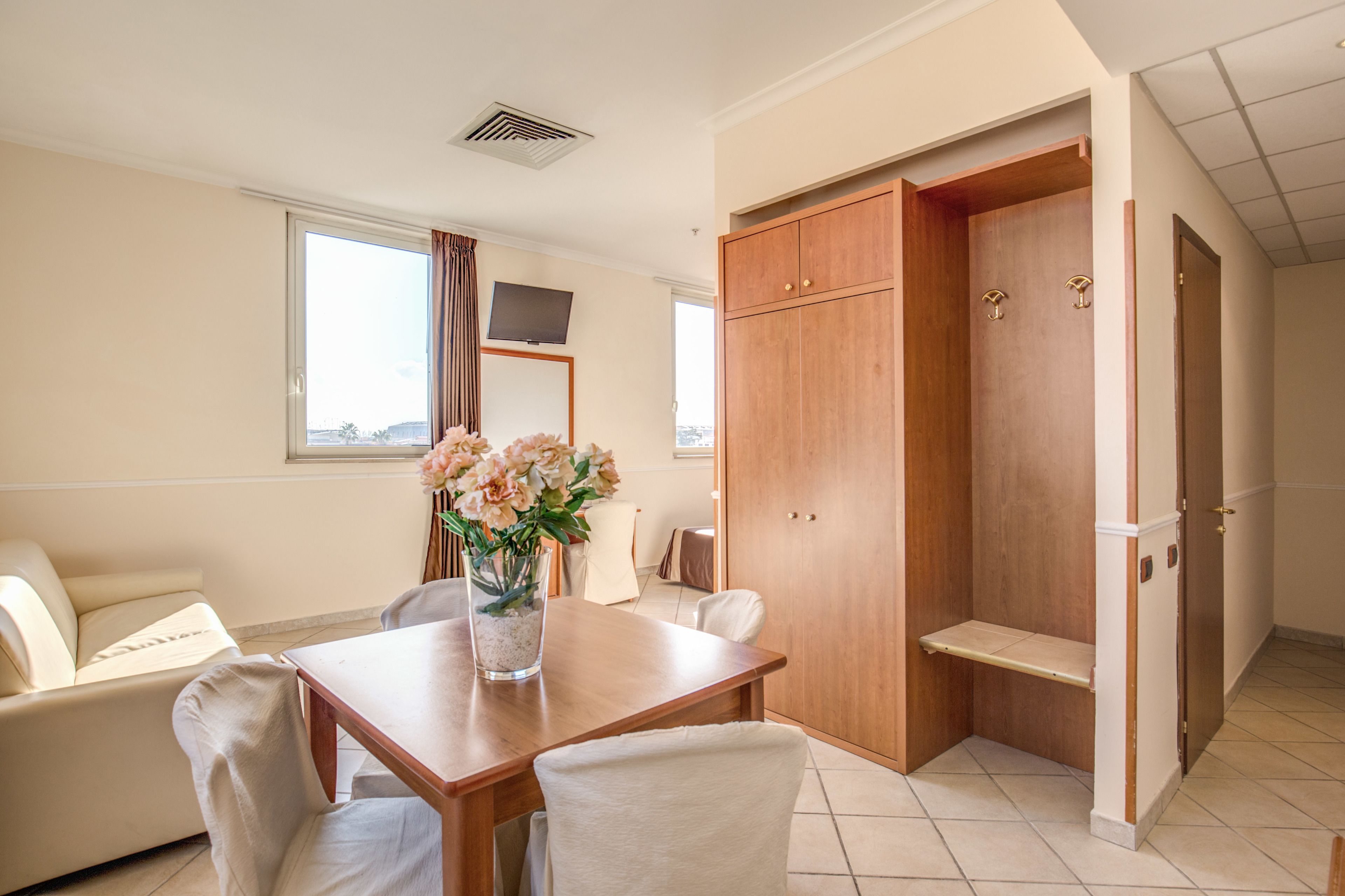 A modern hotel room with a wooden dining table, a sofa, and a large wardrobe.