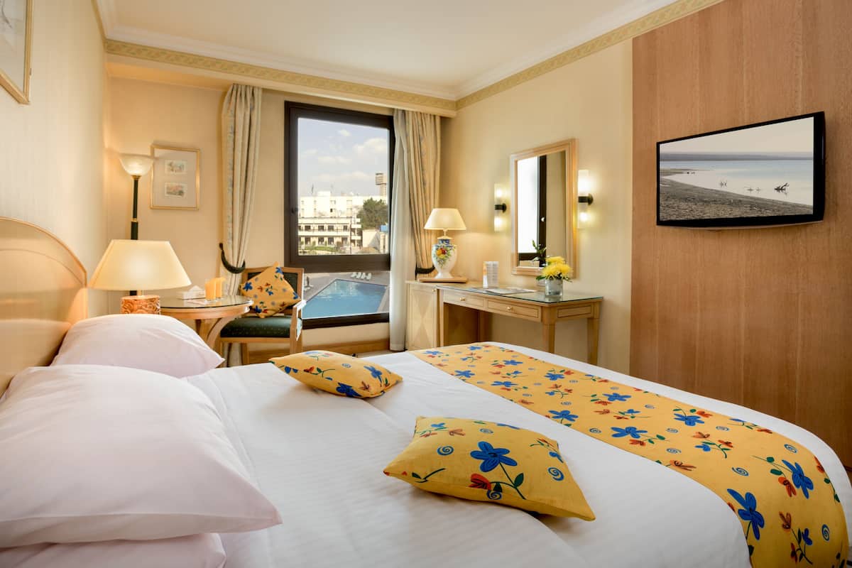 Ein Hotelzimmer mit Bett, Schreibtisch, Stuhl, Fenster mit Blick auf Gebäude und einem Fernseher an der Wand.