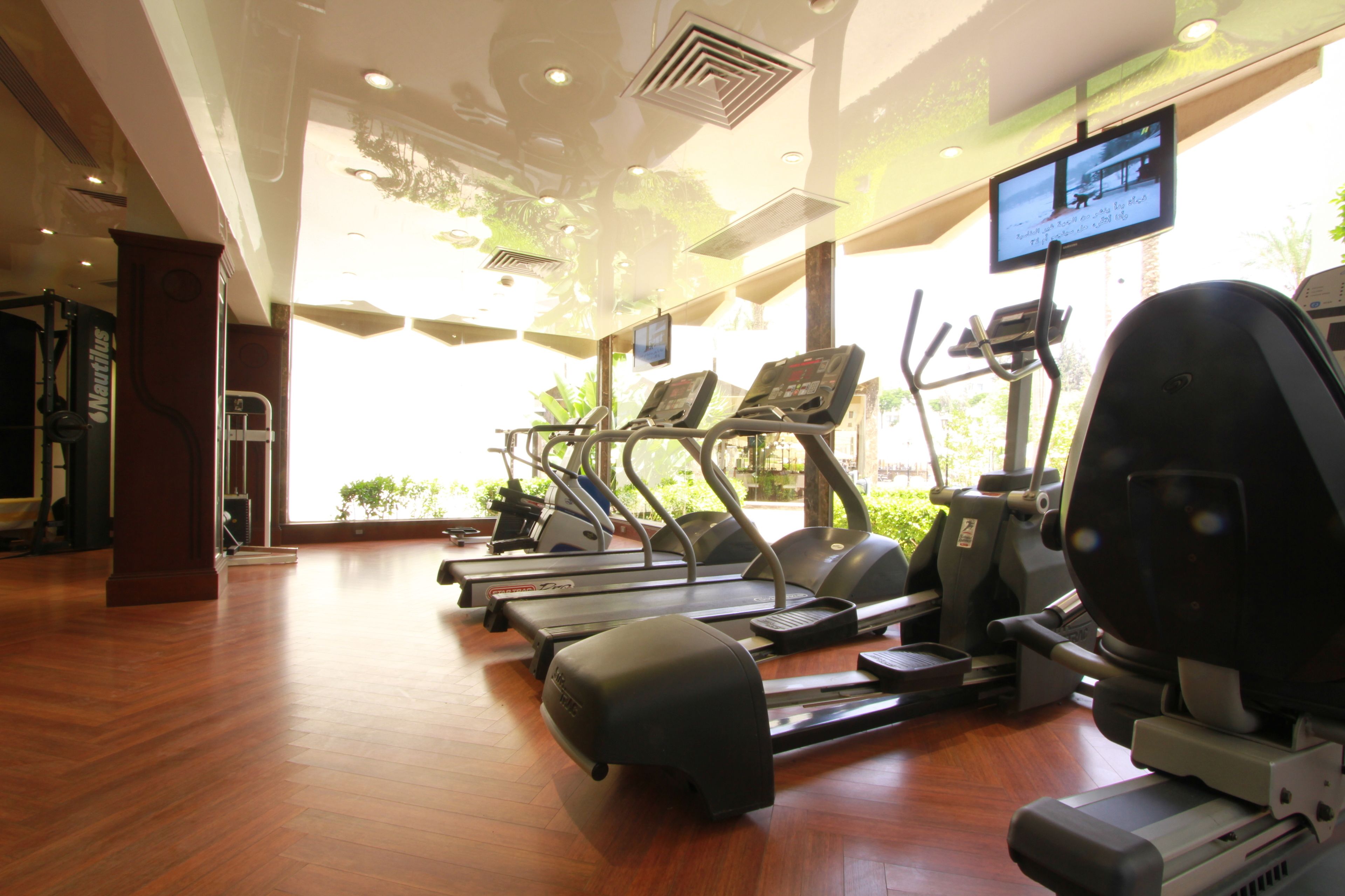 A gym with treadmills, elliptical machines, and a television screen displaying workout videos.