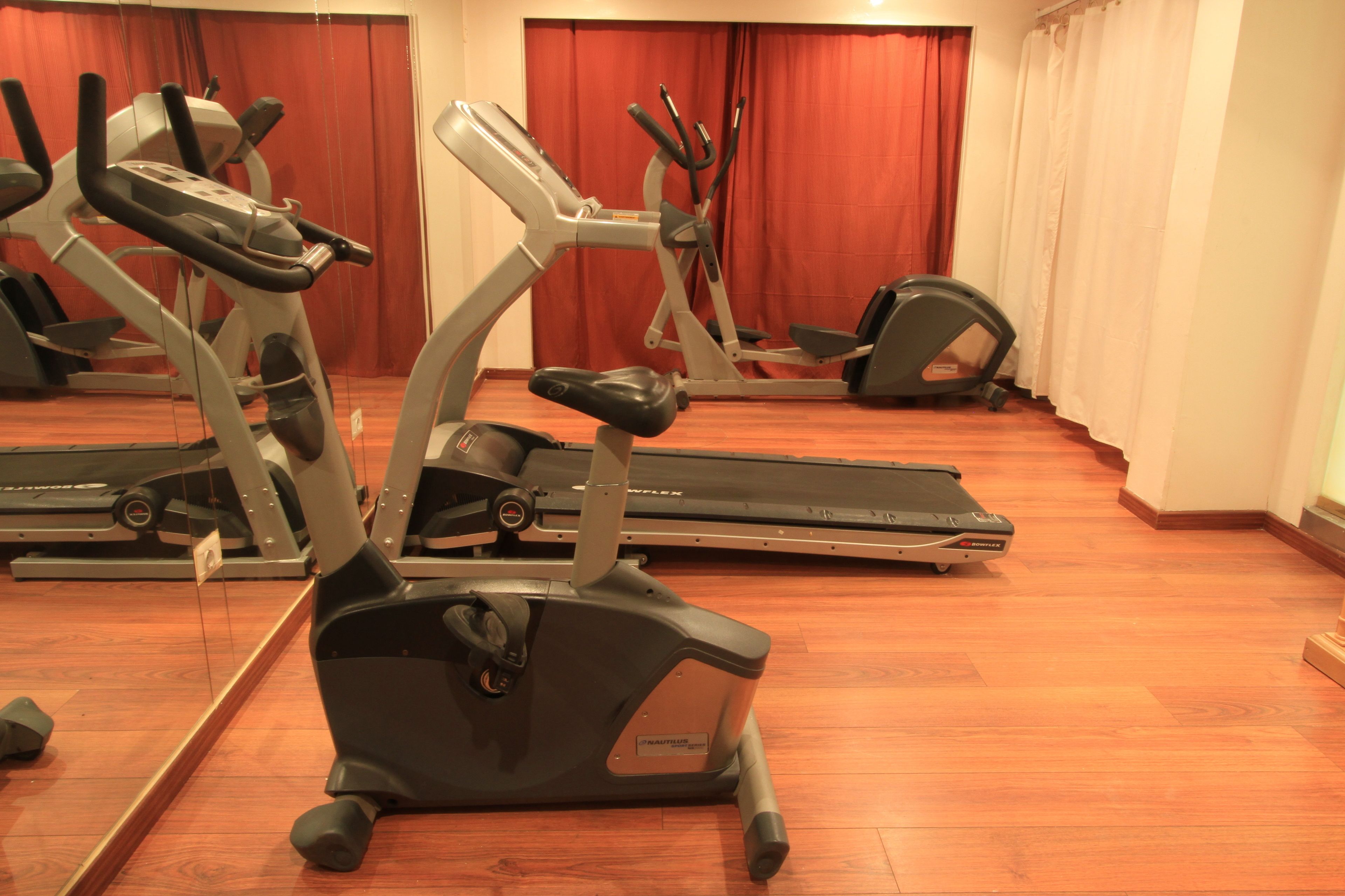 A gym with various exercise machines, including treadmills and elliptical trainers, arranged in a spacious room with wooden flooring.