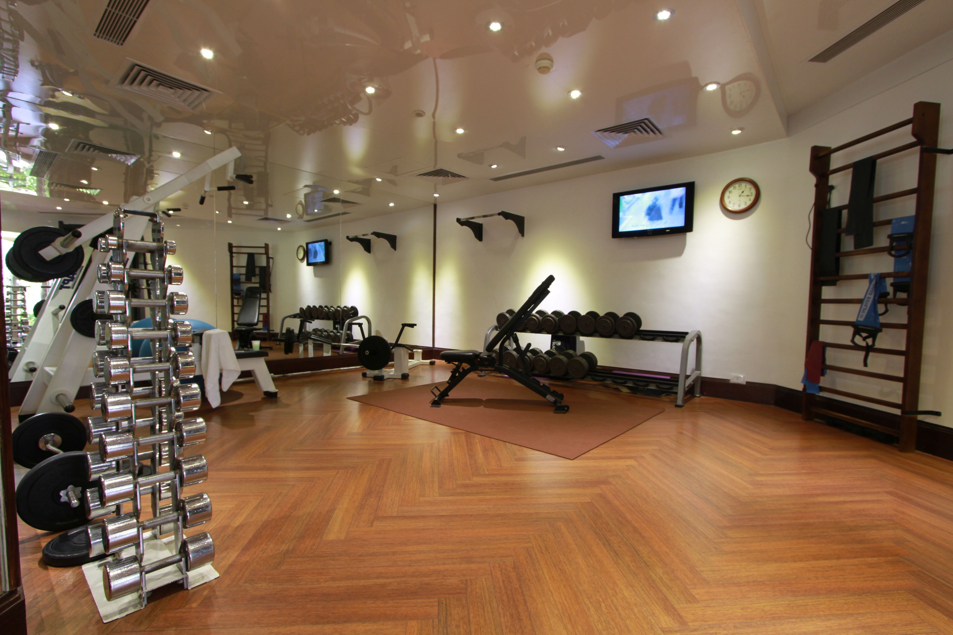 A gym with various exercise equipment, including dumbbells and weight machines, and a television mounted on the wall.