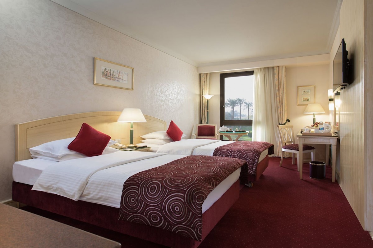 Habitación de hotel con dos camas, un escritorio, una silla, un televisor y una ventana con cortinas.