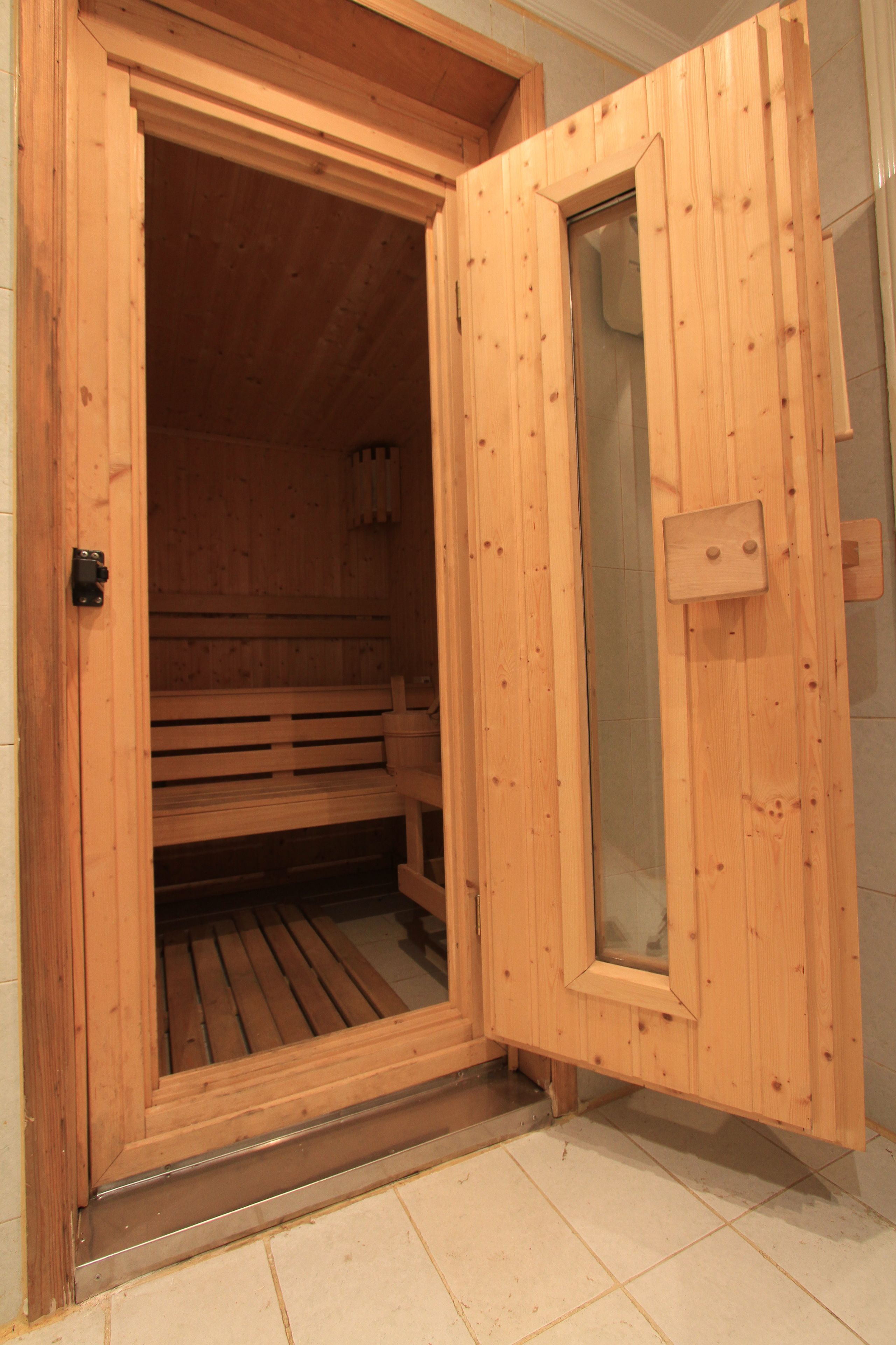Una sauna in legno con una panca all'interno, una porta con un pannello di vetro e un pavimento piastrellato.