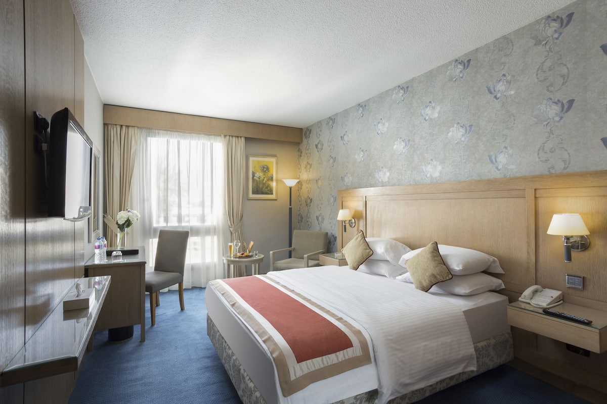 Ein Hotelzimmer mit einem großen Bett, einem Schreibtisch, einem Stuhl, einer Lampe und einem Telefon.