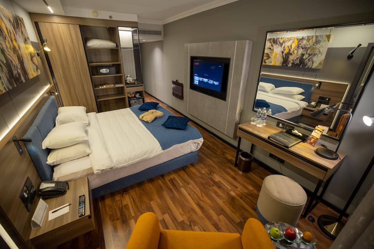 Een moderne hotelkamer met een bed, een bureau, een stoel, een televisie en een kledingkast.